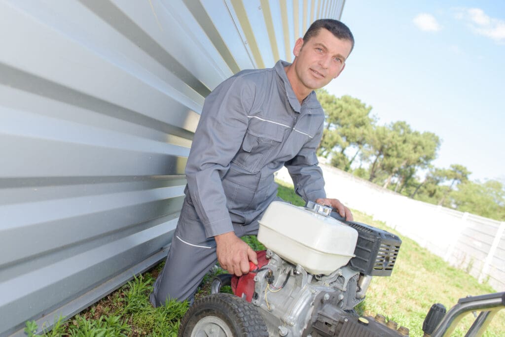 Man kneeling by pressure washer to illustrate Is It OK To Pressure Wash A Metal Roof