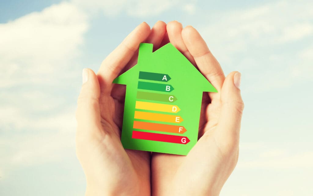 Hands holding a green house cutout with lines of different colors ordered by length to illustrate are metal roofs more energy efficient.