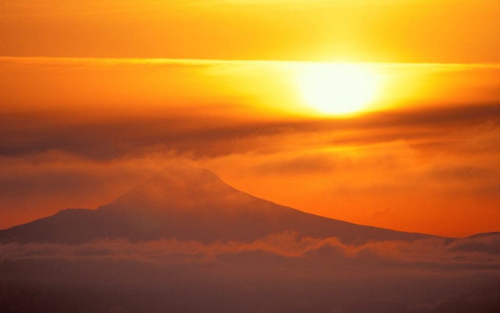 A setting sun near a mountain with an orange sky to help illustrate are black metal roofs hot.