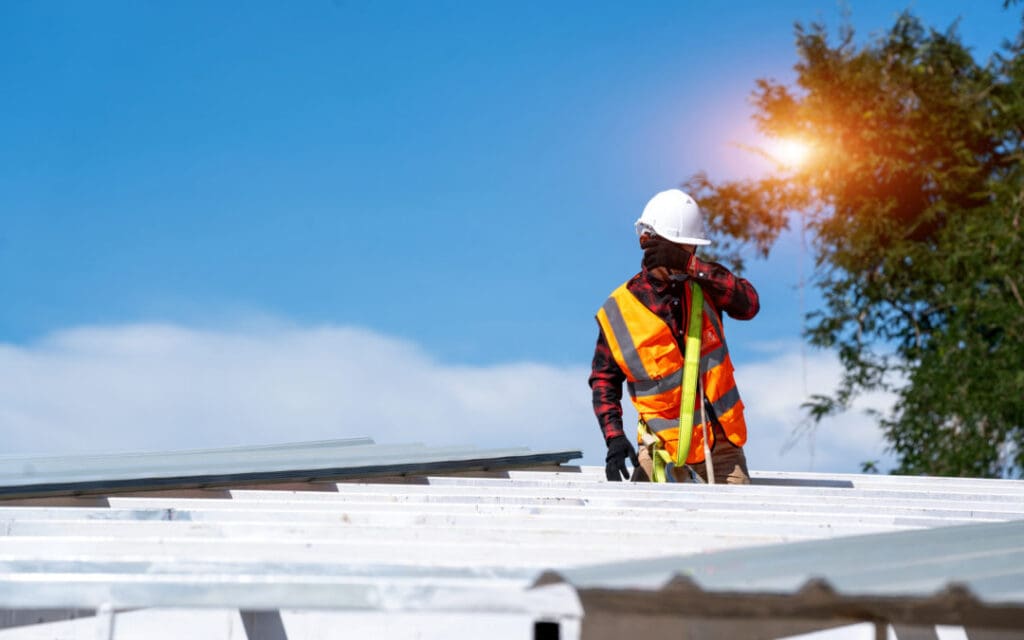 Roofer worker in protective uniform wear and gloves working installing metal sheet on top of the new roof at construction site to help illustrate can you walk on a metal roof